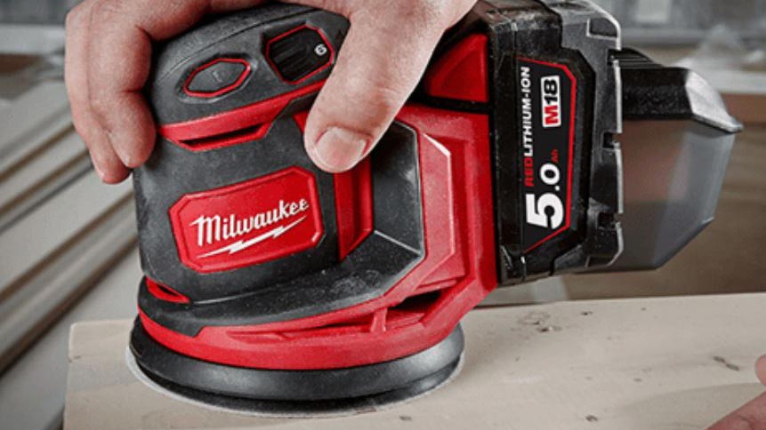 A red and black sander sanding wood