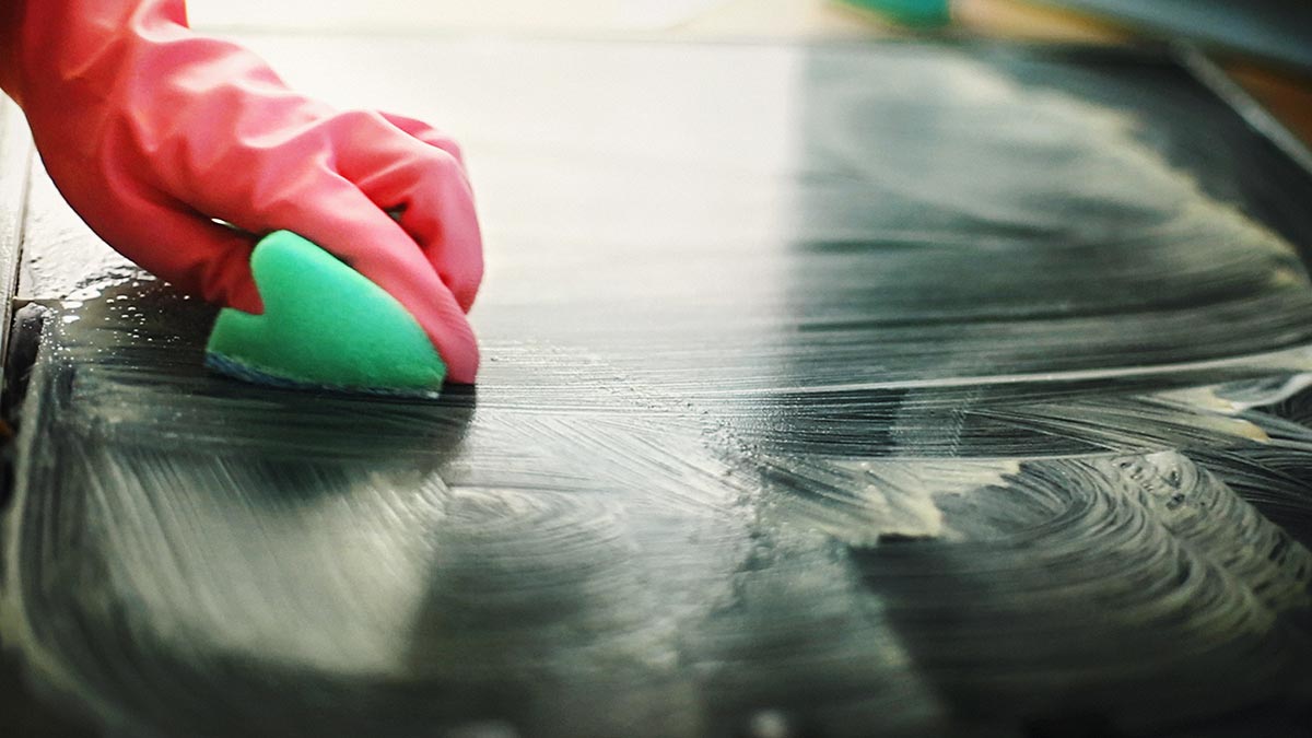 A hand in a rubber glove cleaning a bench top with a sponge