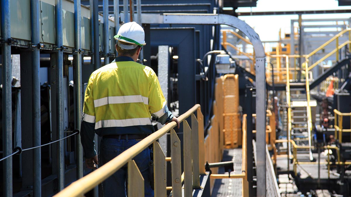 A man wearing high-viz workwear walks along a gantry at a factory